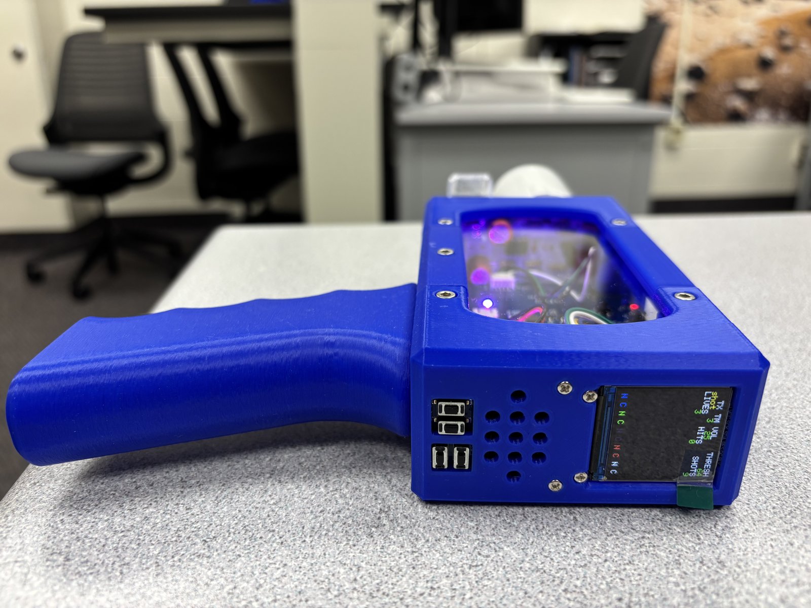Rear of the laser tag gun, showing the grip, buttons, speaker holes and a display listing lives, hits and shots