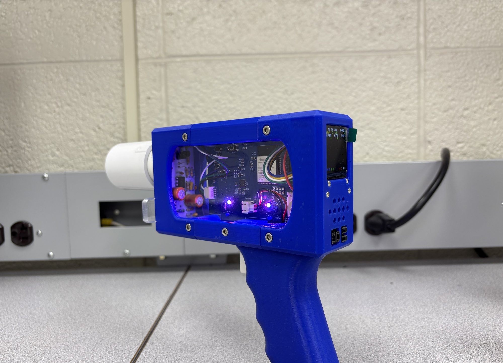 The finished laser tag gun, a blue enclosure with a clear window showing the circuit boards inside, a lens tube on the front and a small display on the back
