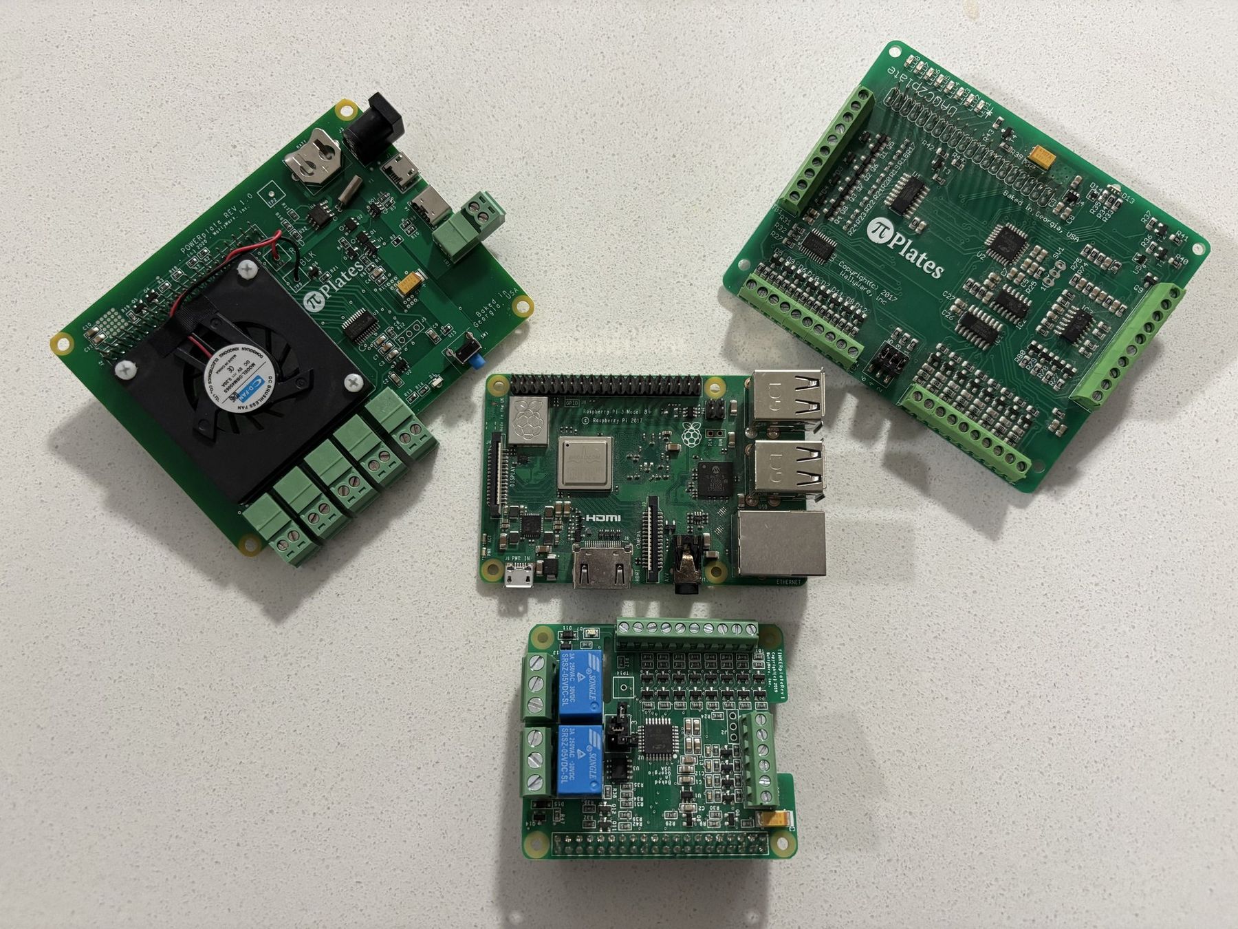 A Raspberry Pi surrounded by three green Pi-Plates expansion boards, laid out on a white countertop