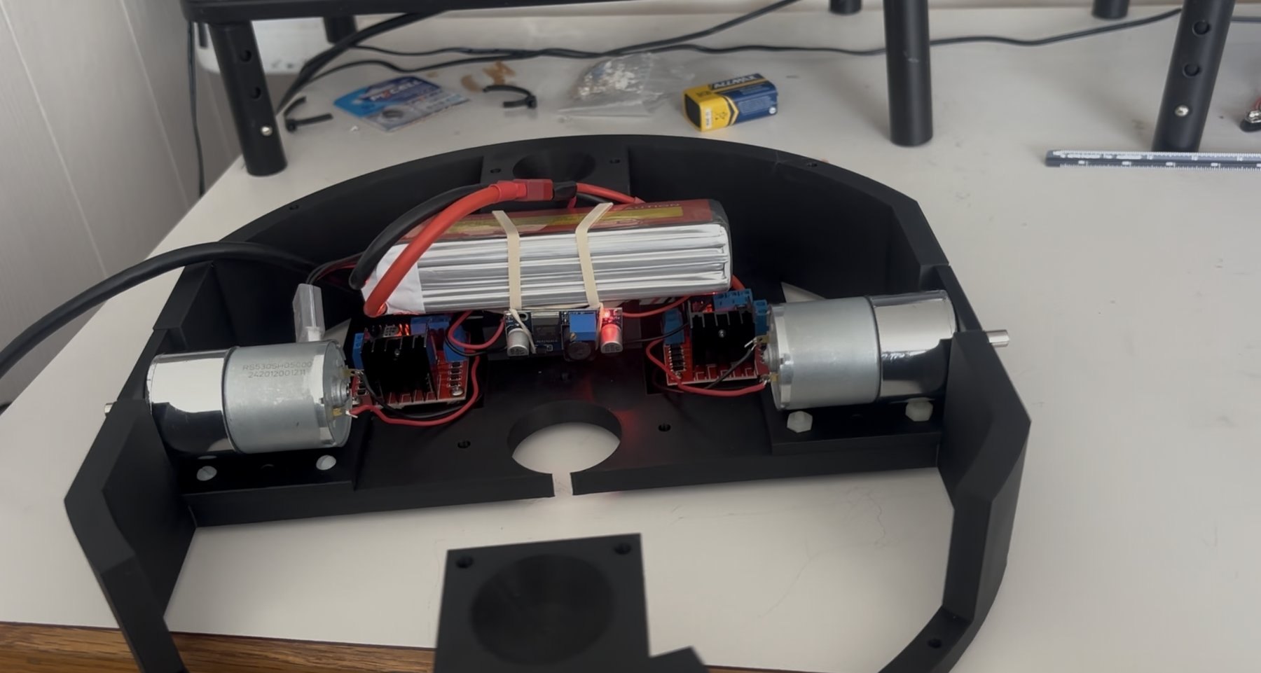 The robot's black 3D-printed chassis with a LiPo battery, two DC gear motors and their motor driver boards mounted inside