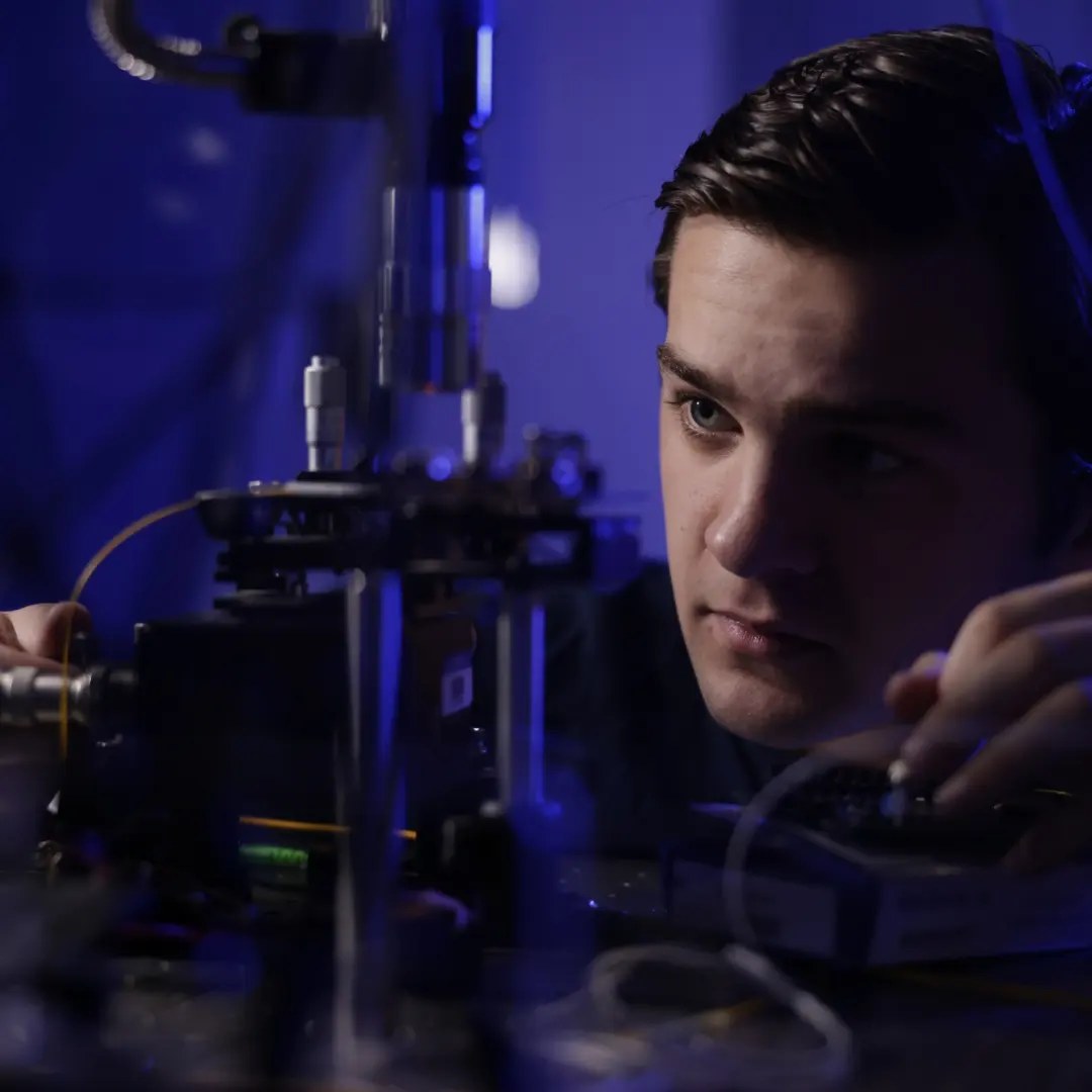 Tyler aligning a fiber to the integrated homodyne QRNG under a microscope